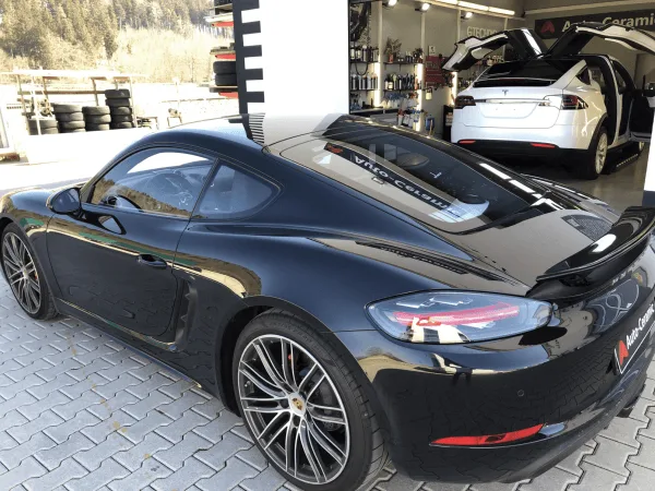 Schwarzer Porsche 718 von hinten, im Hintergrund ein Tesla Model X